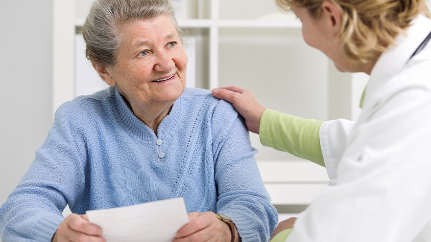 senior woman holding piece of paper with female doctor sitting next to her touching her shoulder