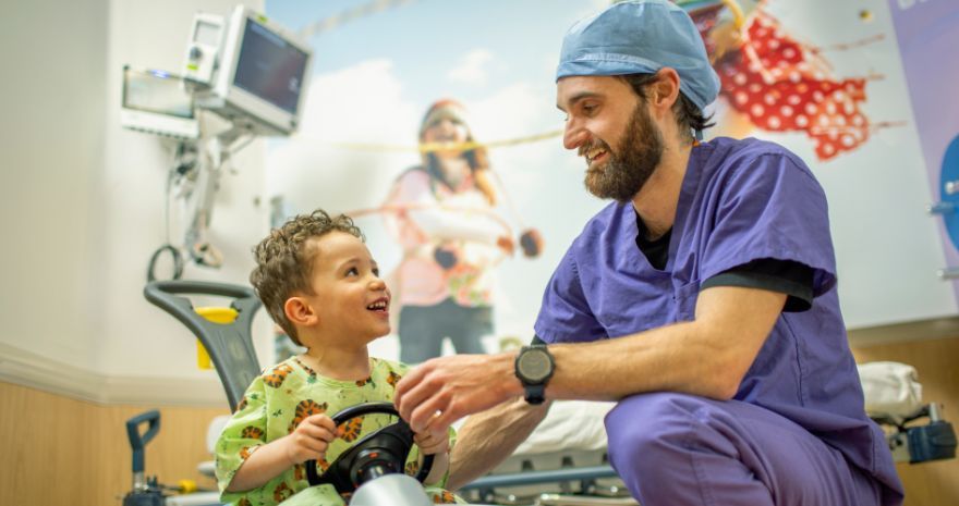 Renown Pediatric nurse smiles at children's hospital patient on toy car