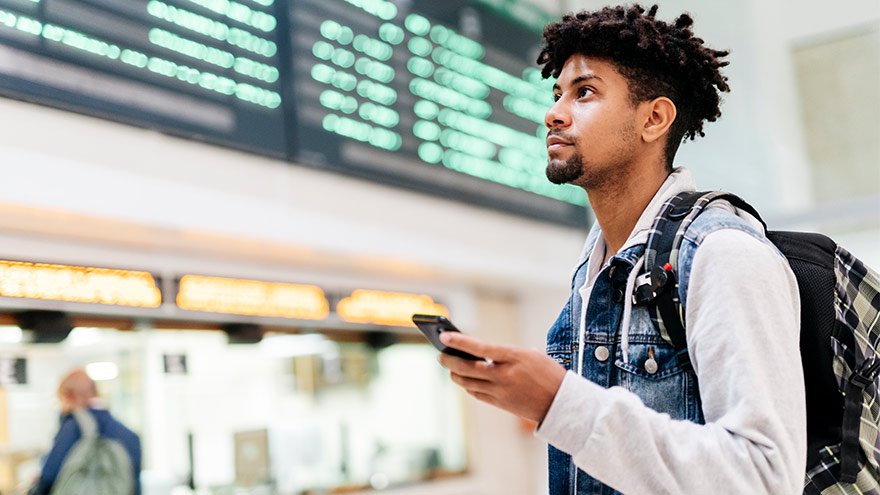 Young man at the airport looking at the list of destinations holding a cell phone