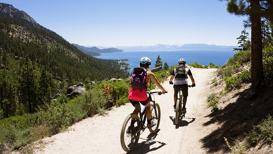 Rear view of cyclists riding bicycles on dirt road against clear blue sky at Lake Tahoe
