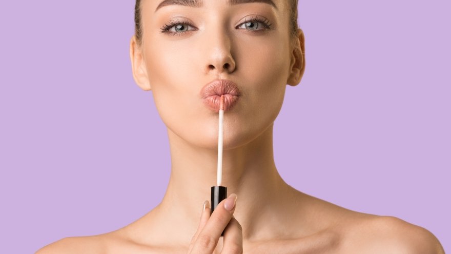 Woman applying lip gloss to pouty lips