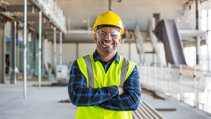 Man in construction vest and hard hat, posing on a site.