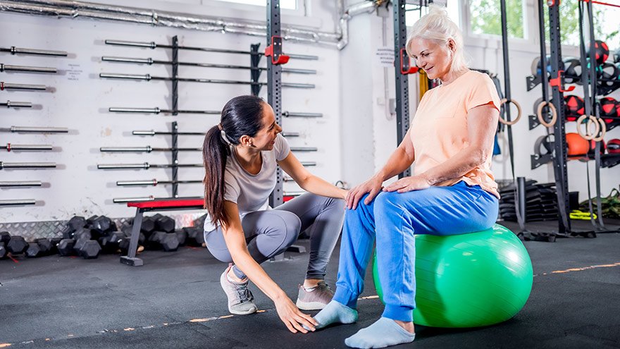 Senior woman with trainer doing rehab using Pilates ball in the rehabilitation center