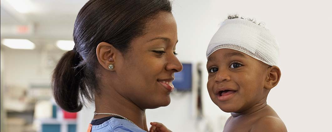 Smiling female nurse holding happy baby with head bandage