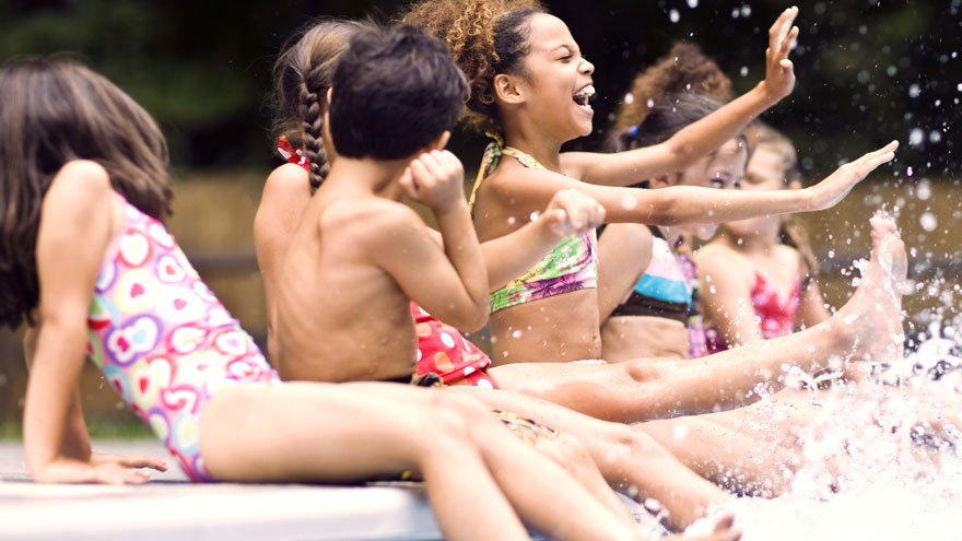 Group of kids sitting on edge of pool, splashing