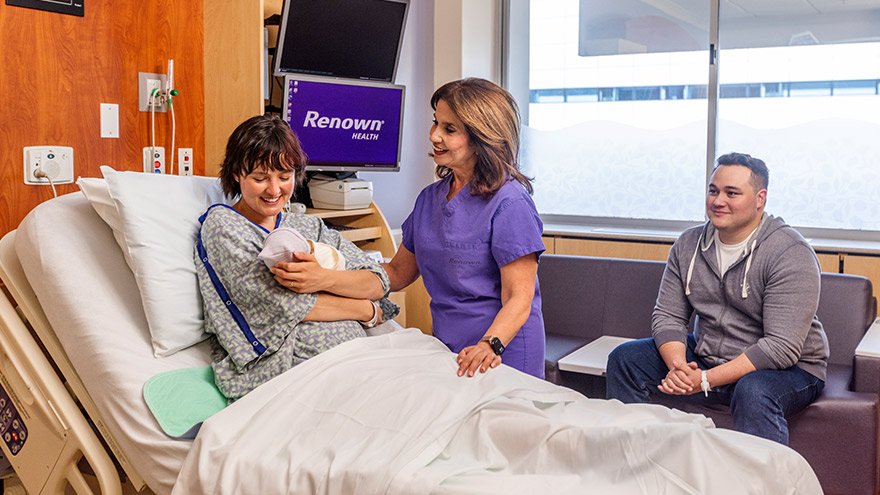 Renown OBGYN Doctor supporting female patient holding newborn baby while father looks on