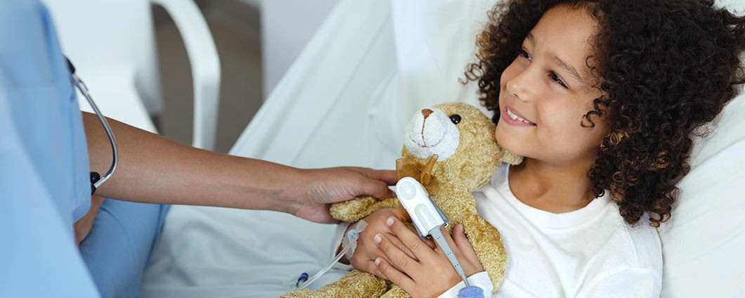 Young patient holding on to teddy bear, smiling at her doctor
