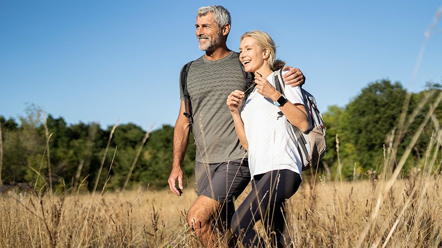Smiling mature couple with backpacks hiking in forest on sunny day