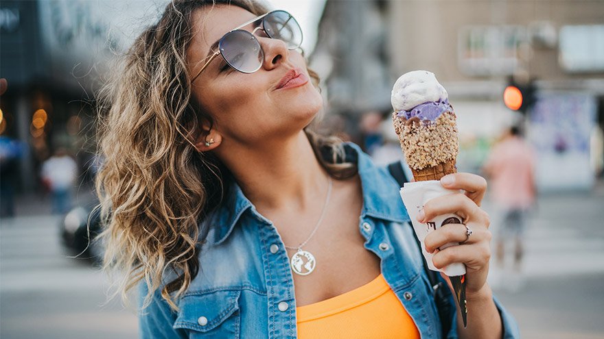 Young woman eating ice cream in the city on sunny summer day