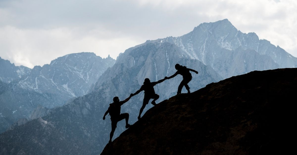 Climbers helping each other up a mountain ridge