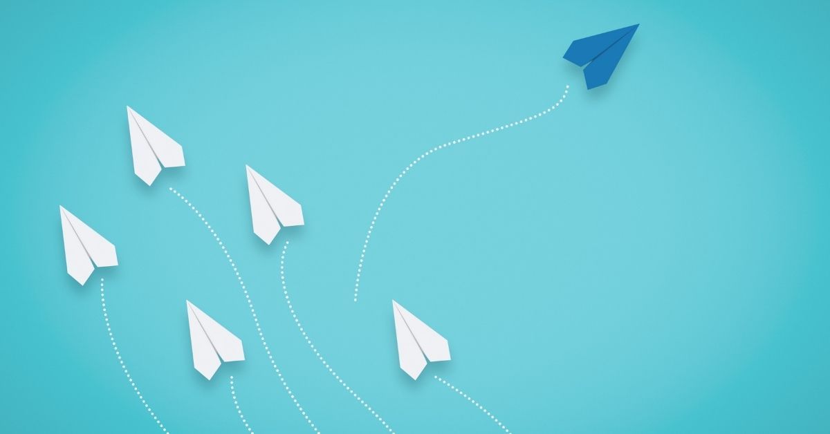 A blue paper plane charting its own course away from the flock