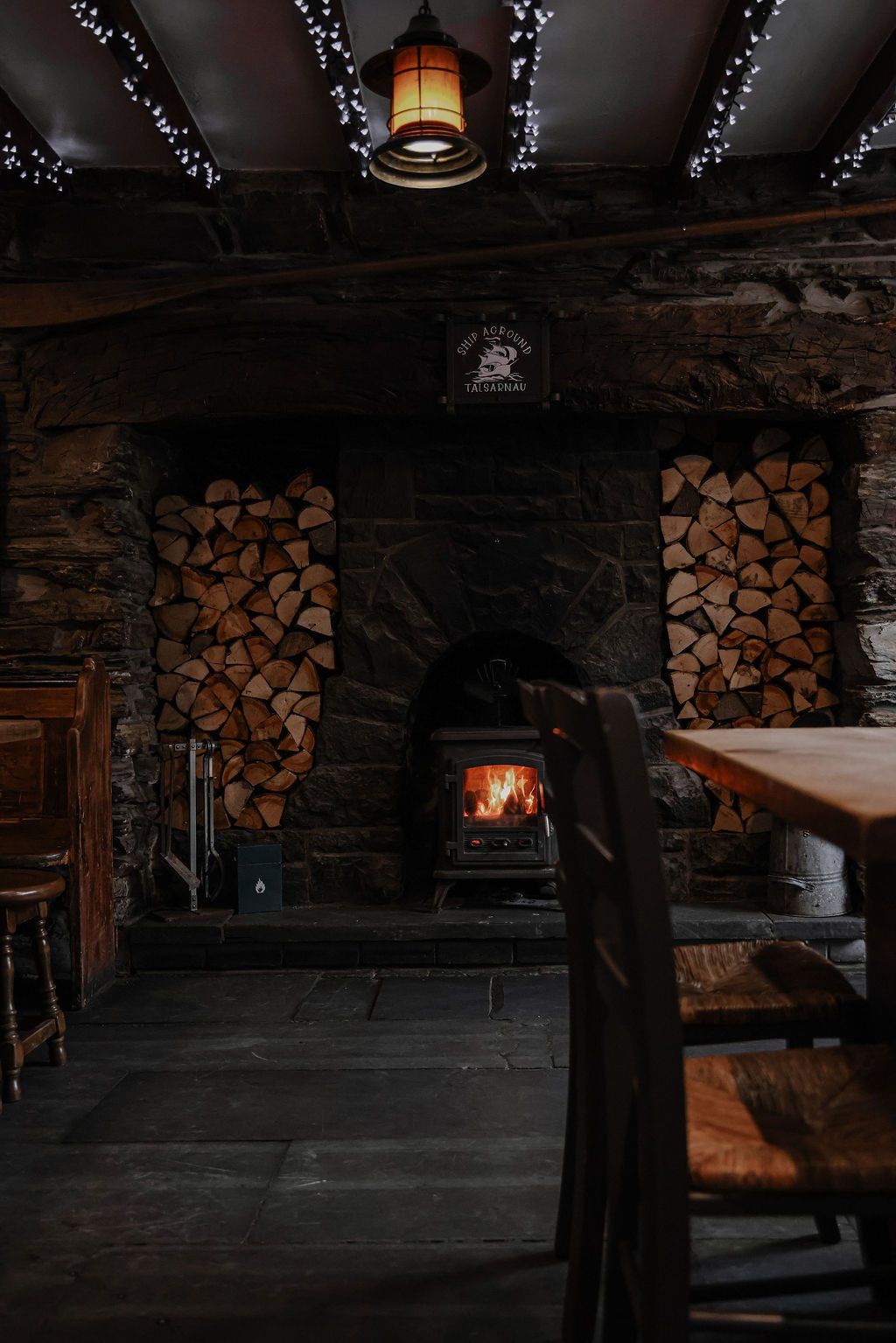 A wood-burning stove burning low beneath stacked logs
