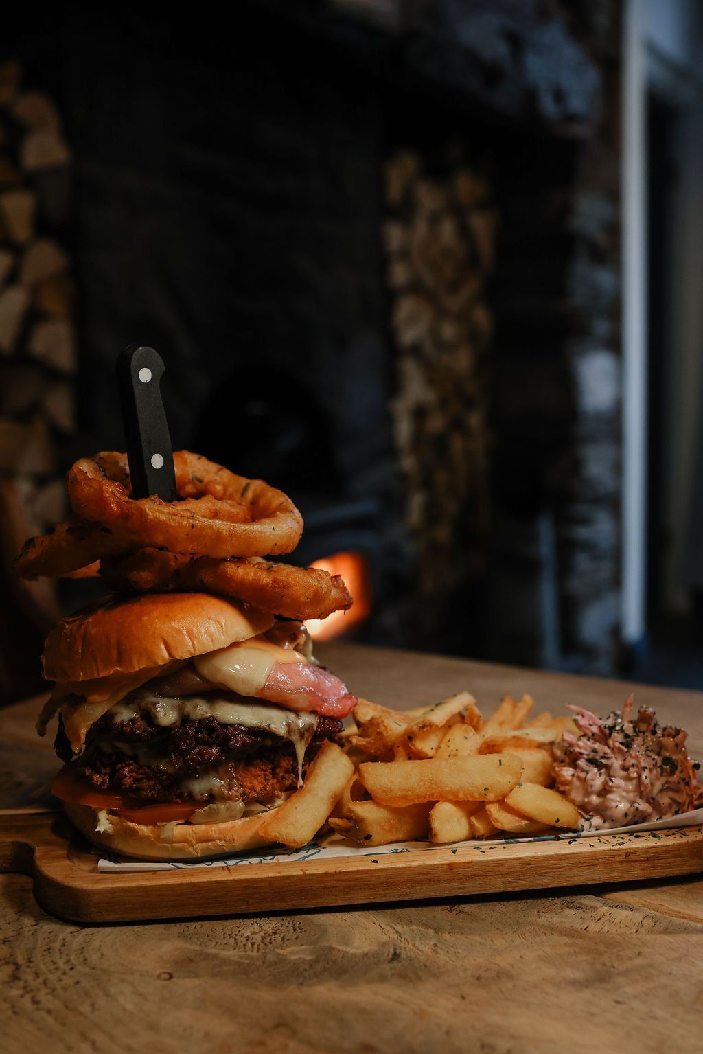 A loaded burger with onion rings and fries on a board