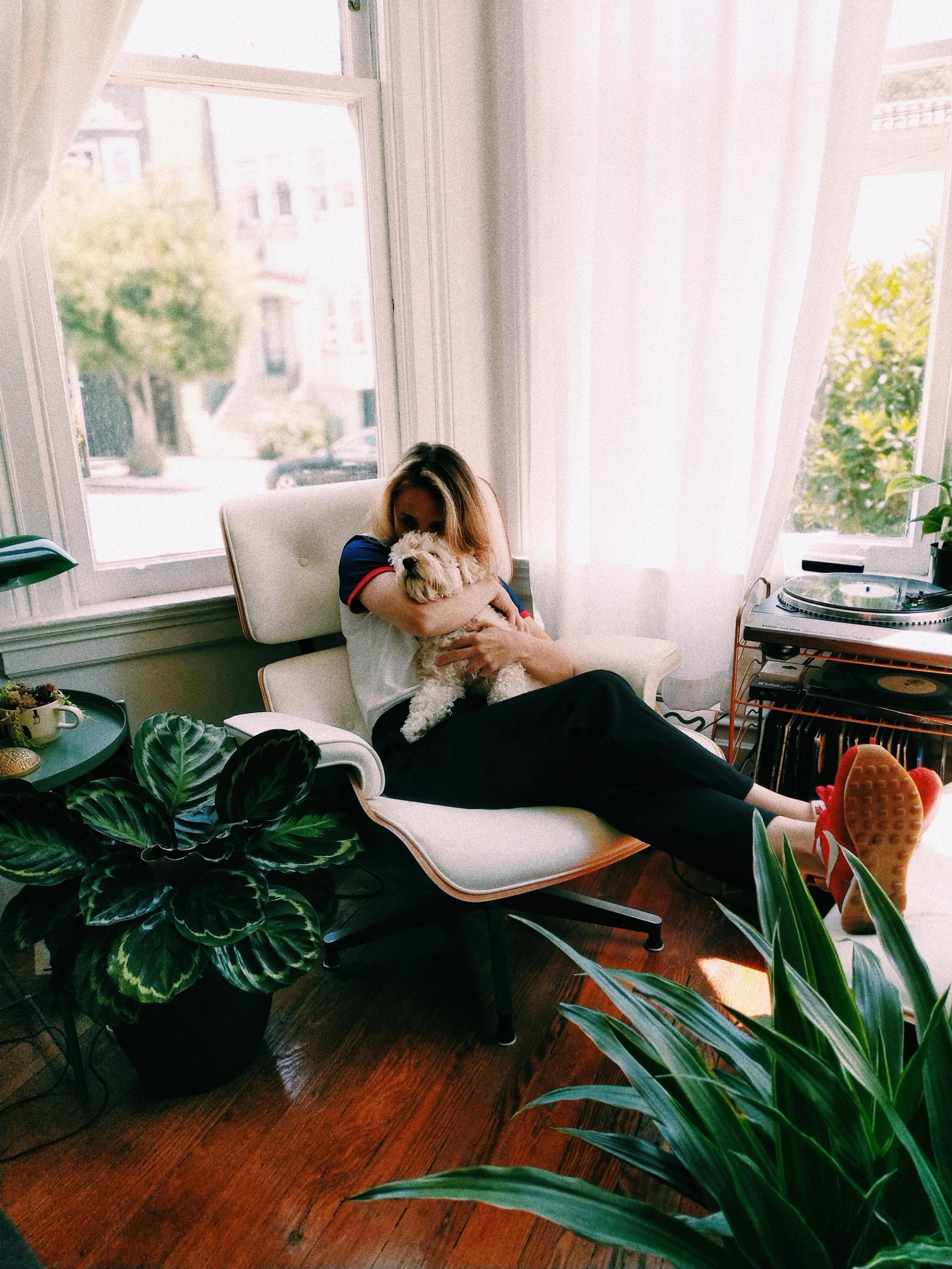 Woman holding a dog while sitting on a chair in a light room filled with plants