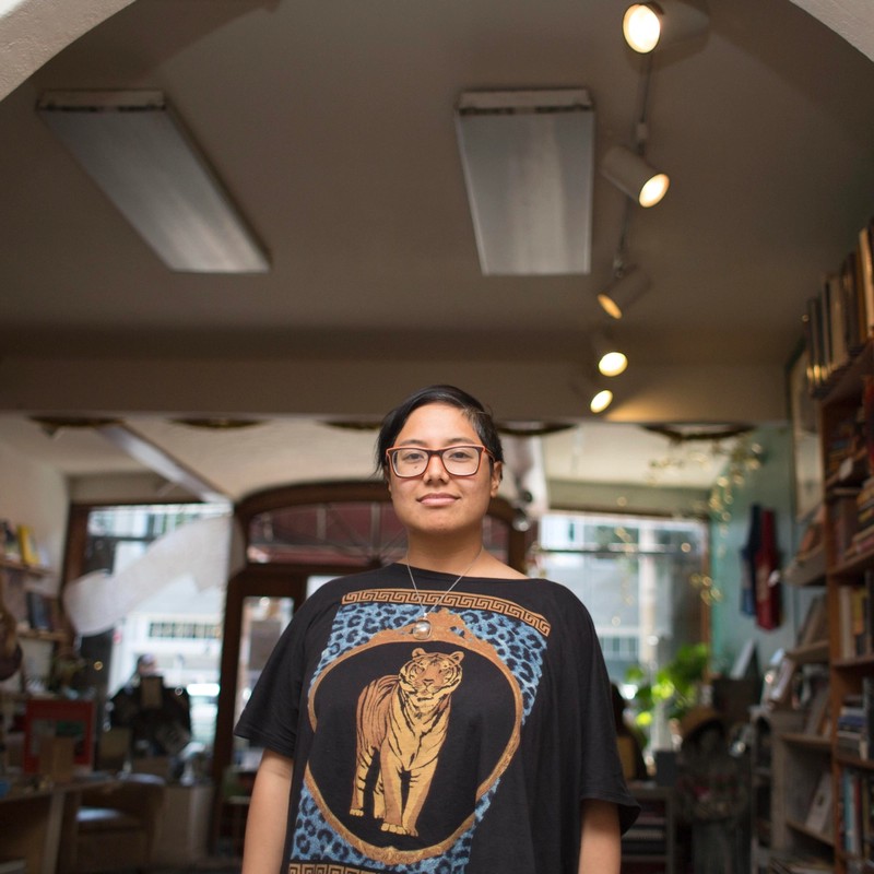 Image of Dorothy R. Santos with short dark hair, wearing black and orange glasses and a shirt with a tiger print under an archway inside a bookshop.