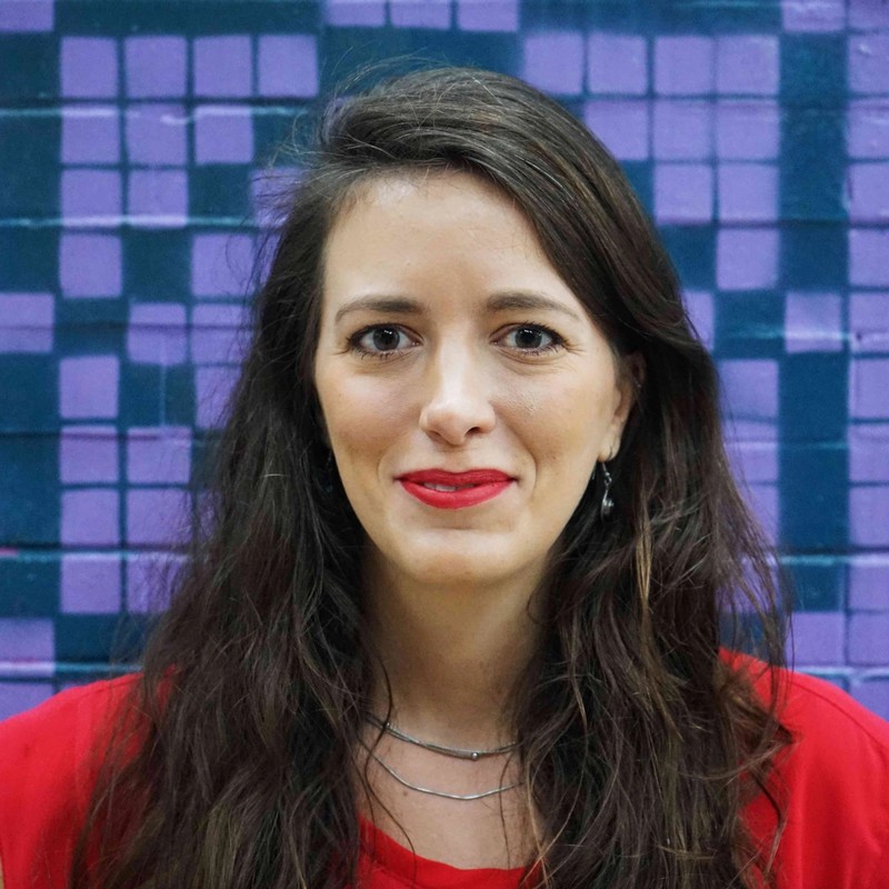 Headshot of Julie, with long brown hair, brown eyes, wearing a red shirt, in front of a purple and green background.