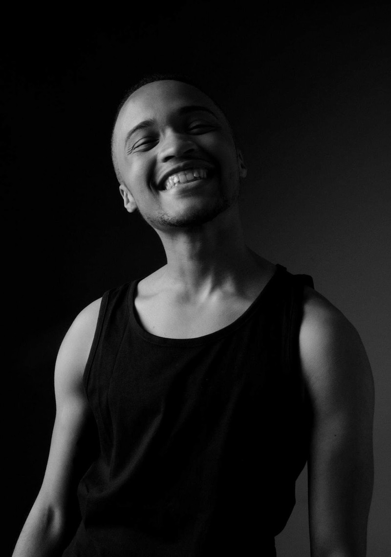 Black and white Half body shot of Cydney Brown in a black tank top, smiling with their head tilted back. 