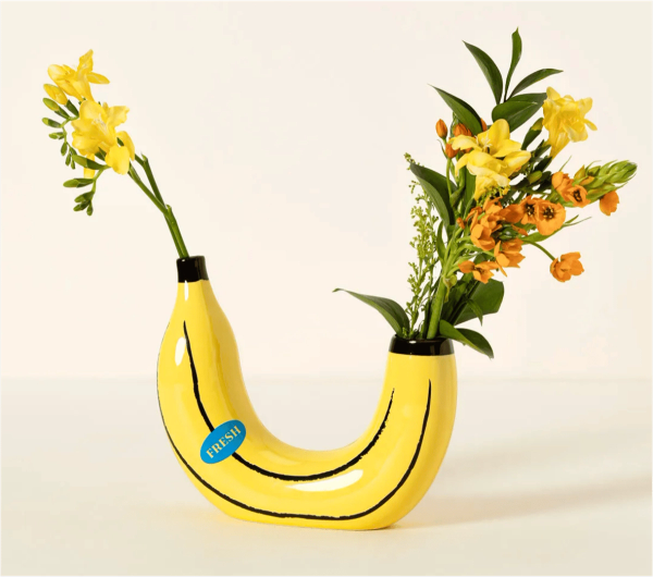A glossy yellow banana-shaped ceramic vase holding yellow and orange flowers.
