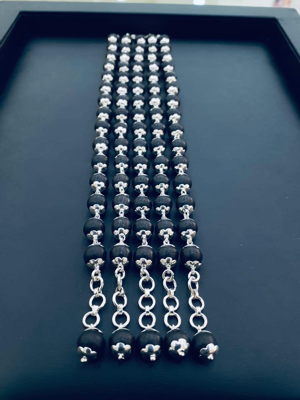 Five identical chains of matte black spherical beads with silver-toned floral caps and terminal link chains on a dark background