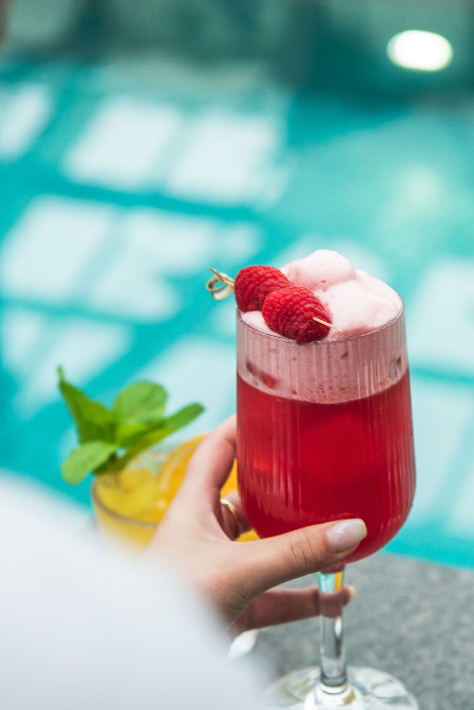 Hand som håller ett vinglas med halloncocktail och skum.