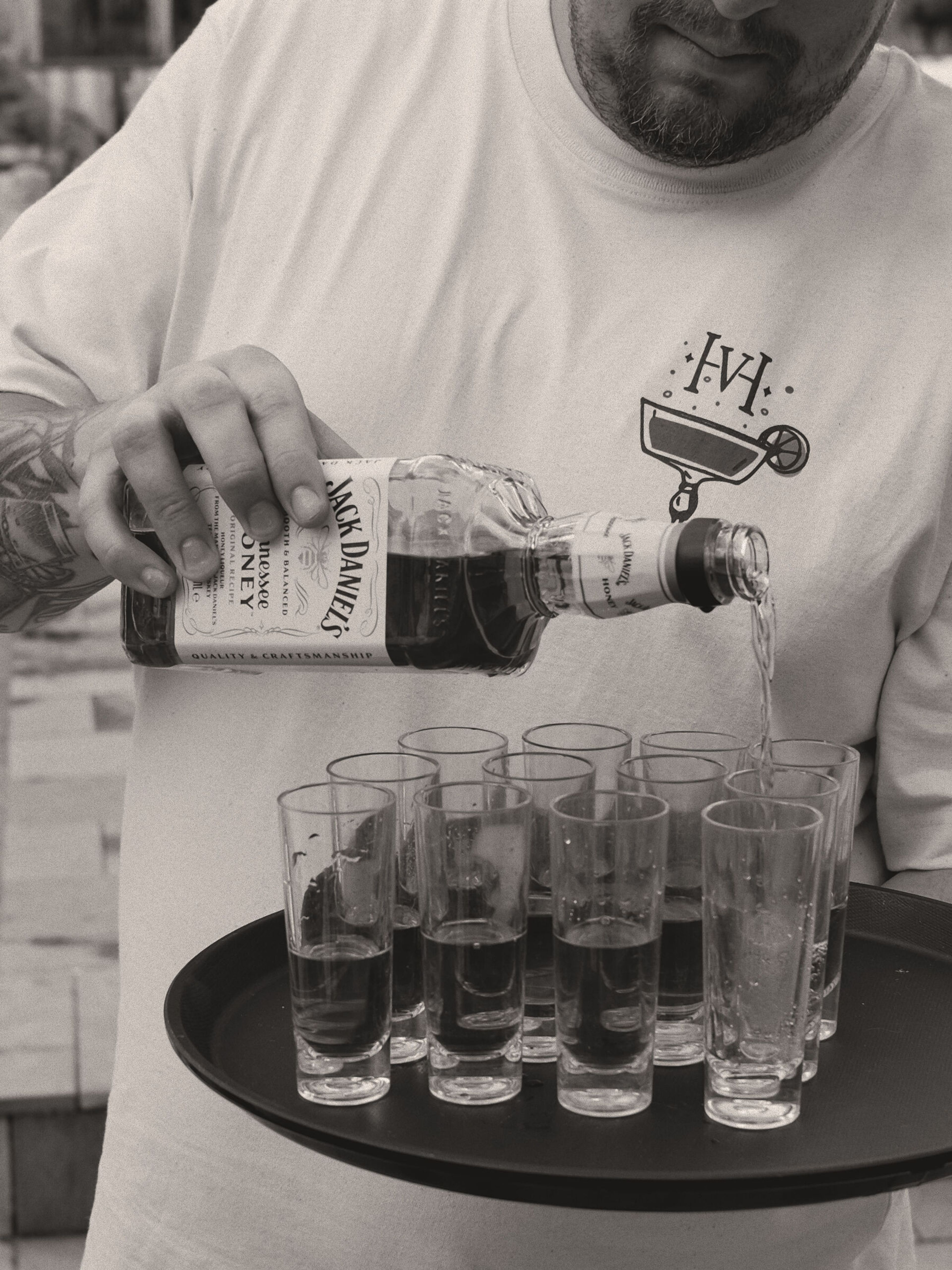 Person häller whiskey från en flaska i höga shotglas på en serveringsbricka.