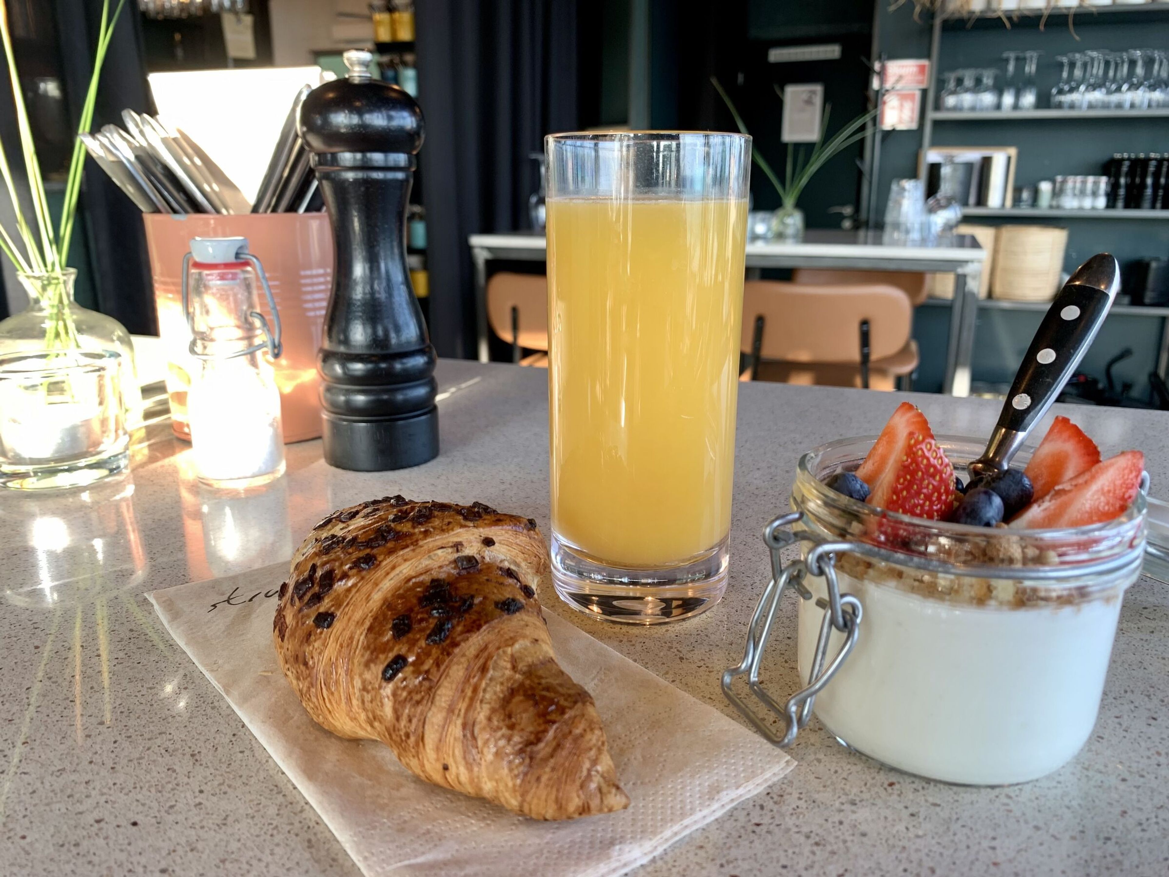 Högt dricksglas med apelsinjuice serverat med croissant och yoghurt.