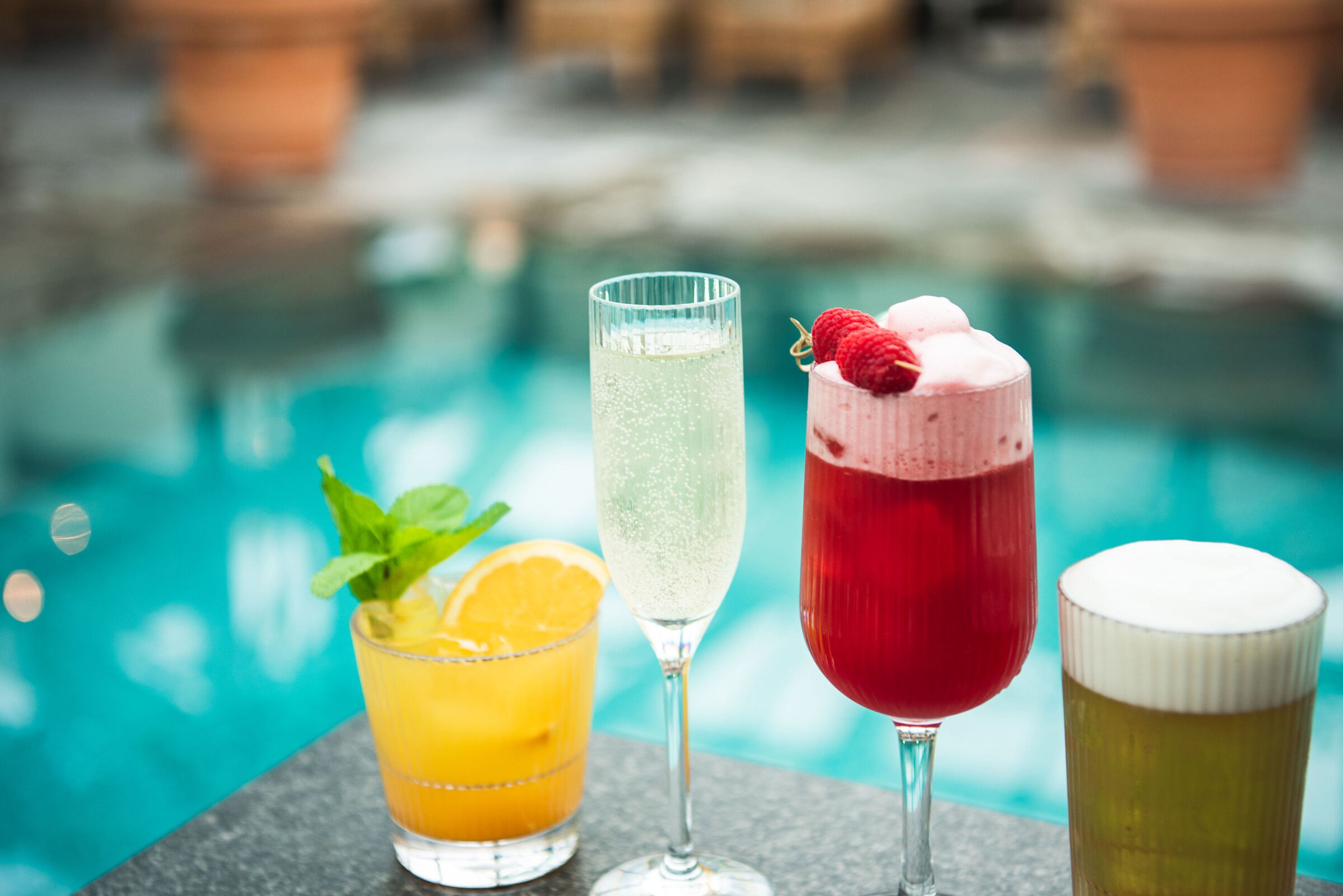 Fyra cocktails i olika glas på ett bord vid en pool.