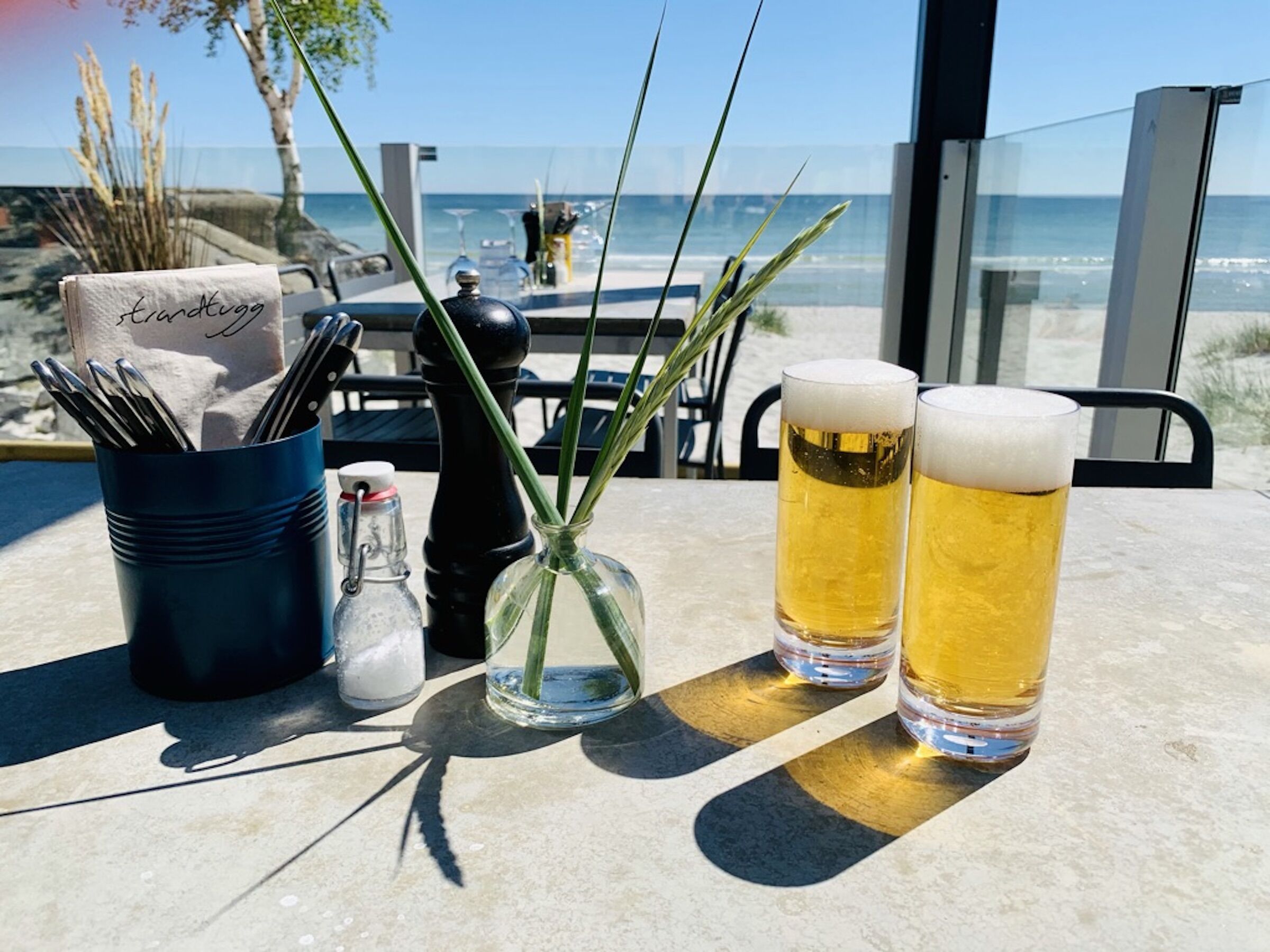 Två öl i höga glas på ett utomhusbord vid havet.