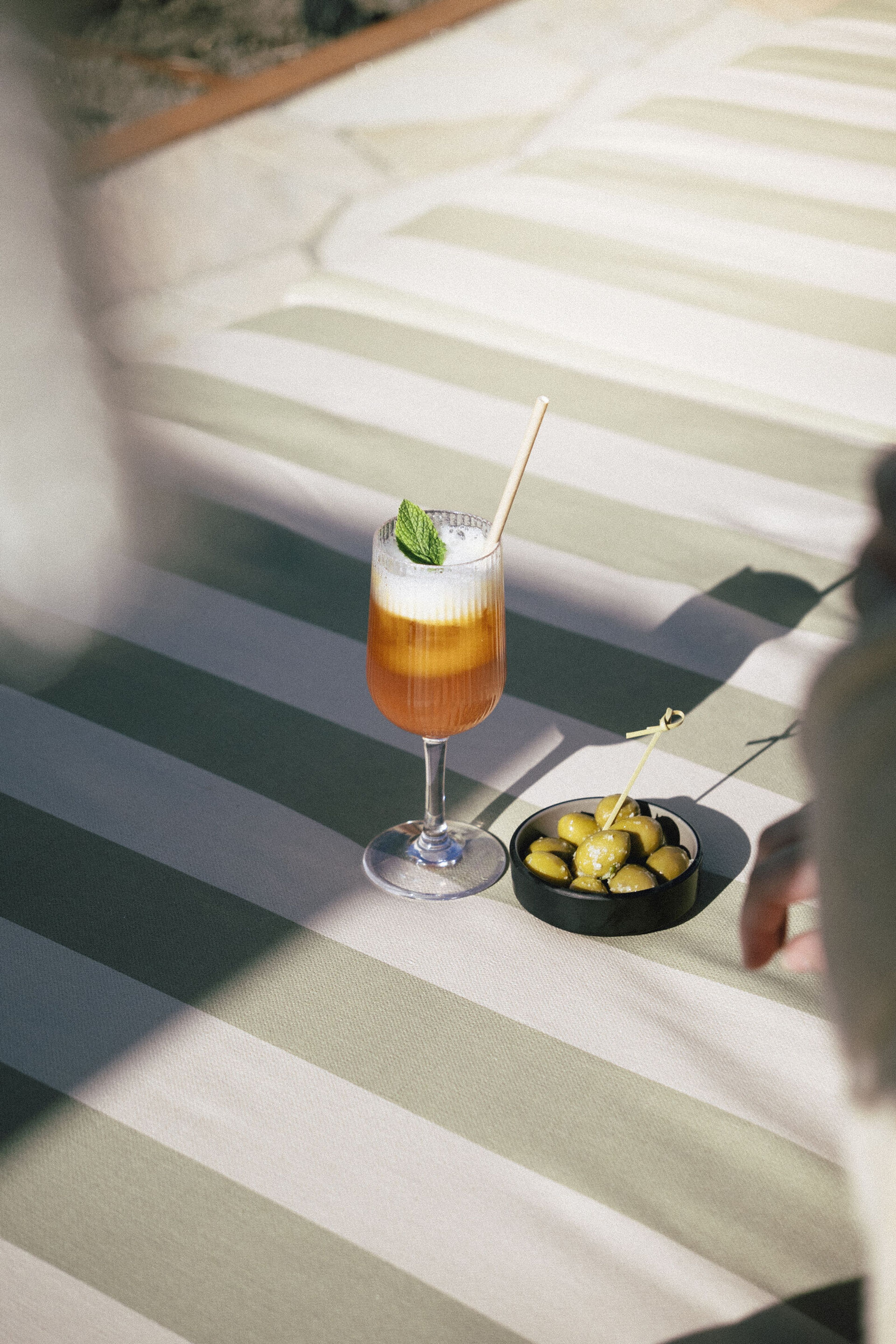 Orange cocktail i ett glas med fot och skum, bredvid en skål med oliver.