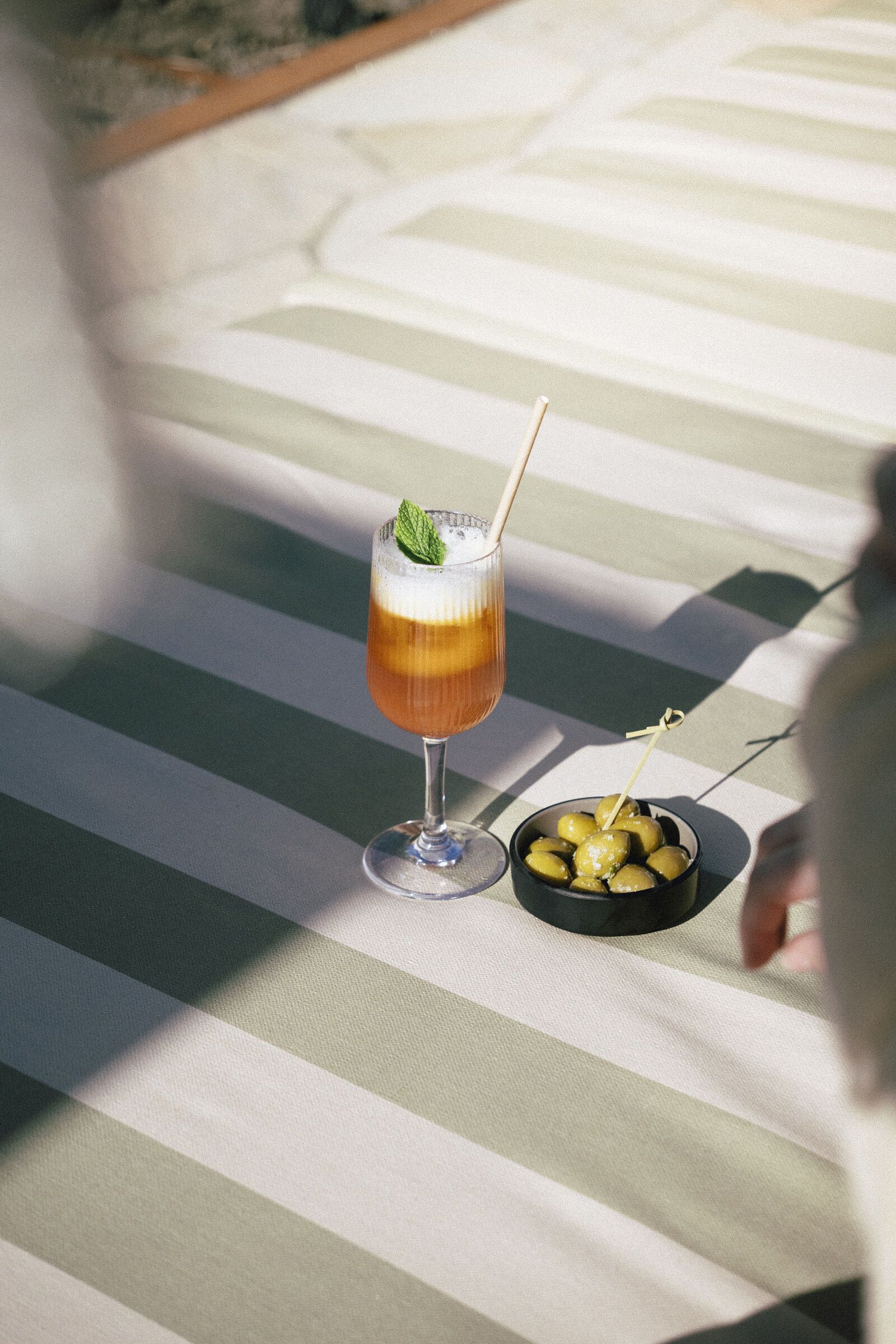 Orange cocktail i ett glas med fot och skum, bredvid en skål med oliver.