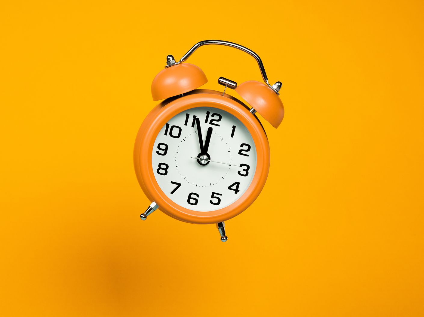 An orange alarm clock on an orange background.