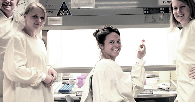 people in lab coats smiling at the camera holding up test results in a test tube