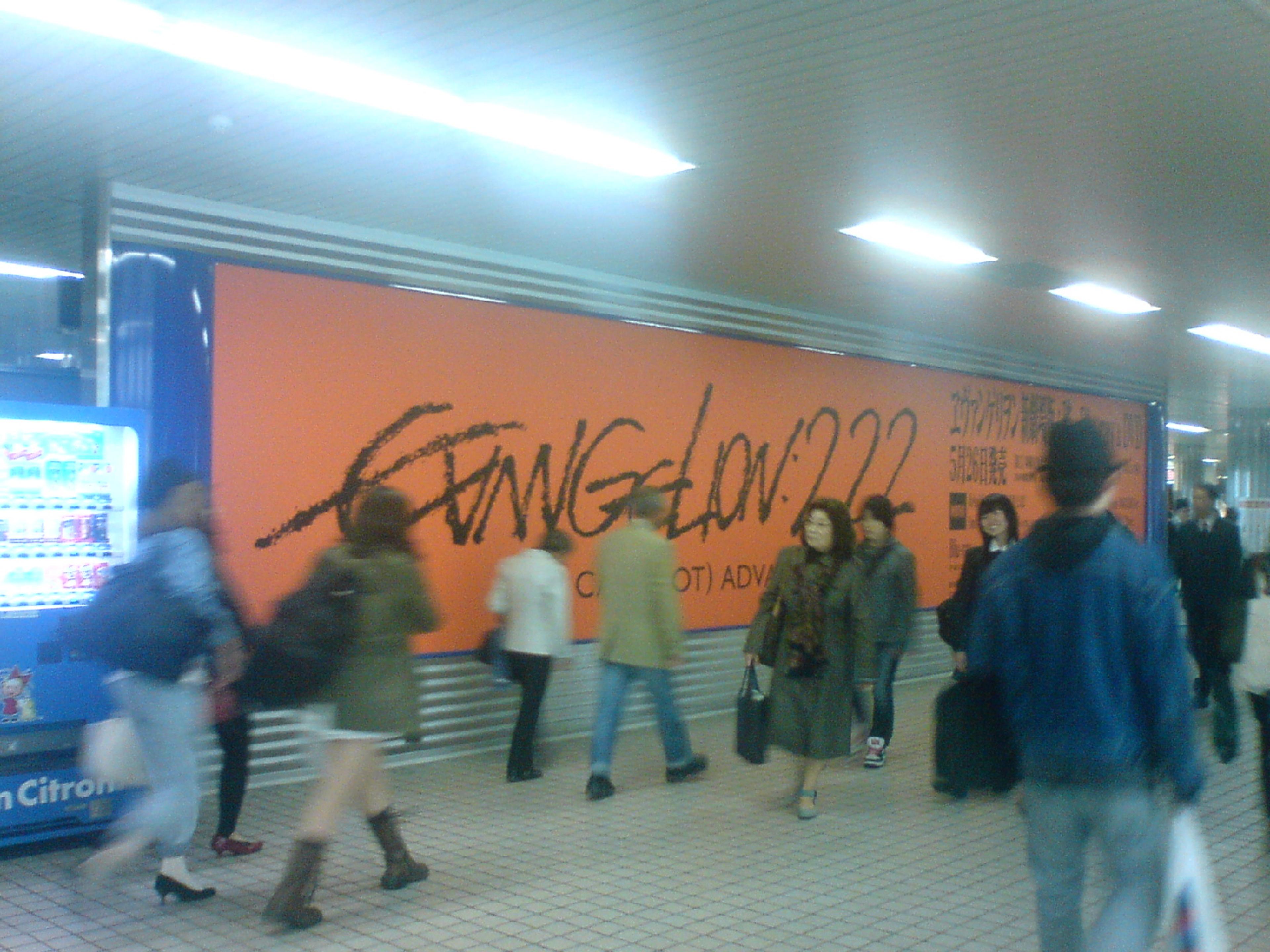 Commuters walking past a large orange Rebuild of Evangelion advertisement on the wall of Odori subway station in Japan