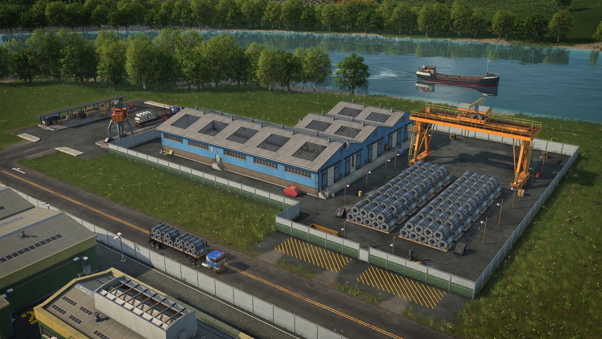 A fenced warehouse yard beside a river, with a blue shed, rows of steel coils on asphalt, yellow hazard markings, an orange gantry crane and a modern semi-trailer leaving with a load of coils.