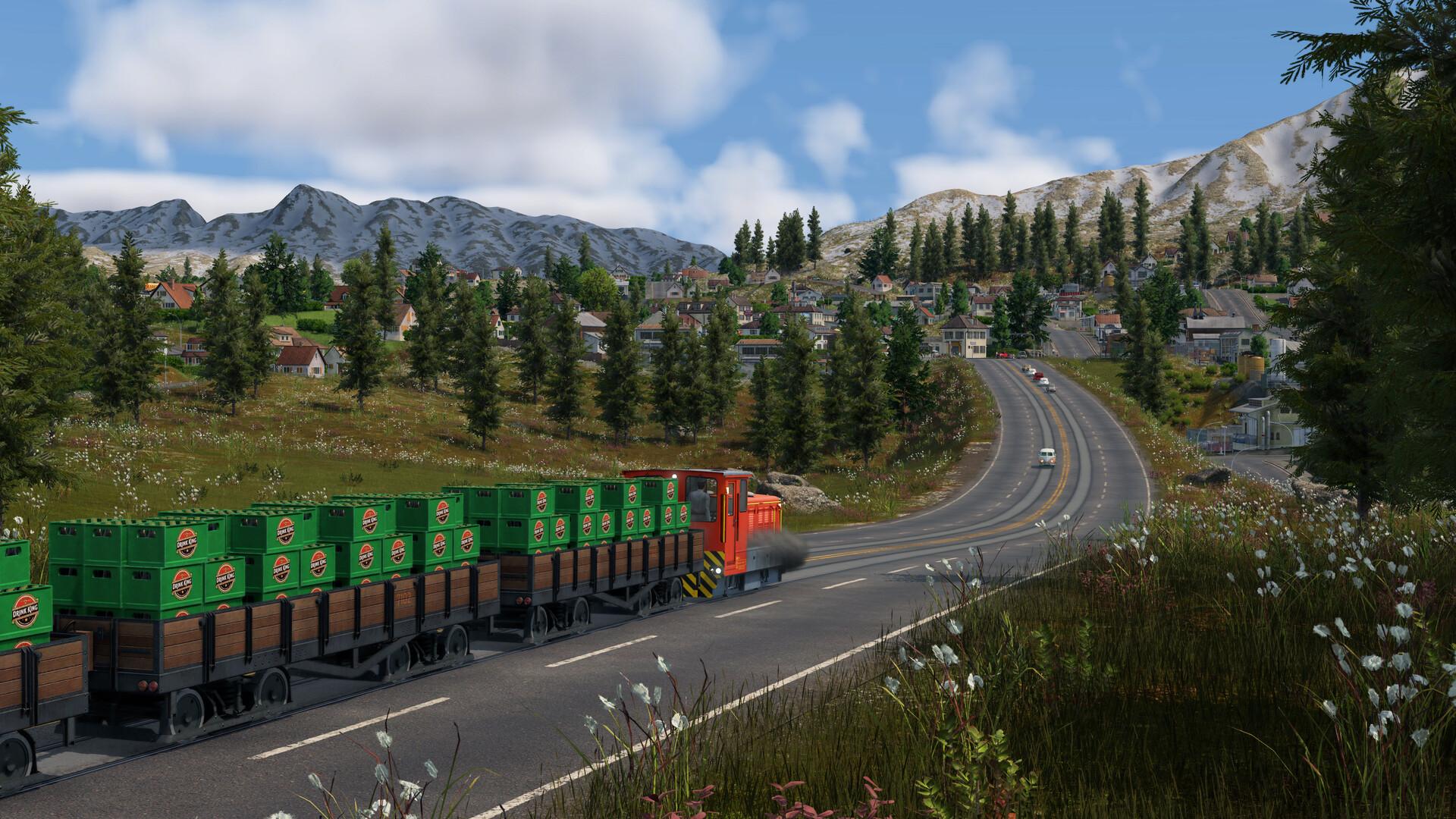 A small orange locomotive pulls flat wagons stacked with green drink crates along tram tracks set into a mountain road, with a hillside town and snow-dusted peaks behind.