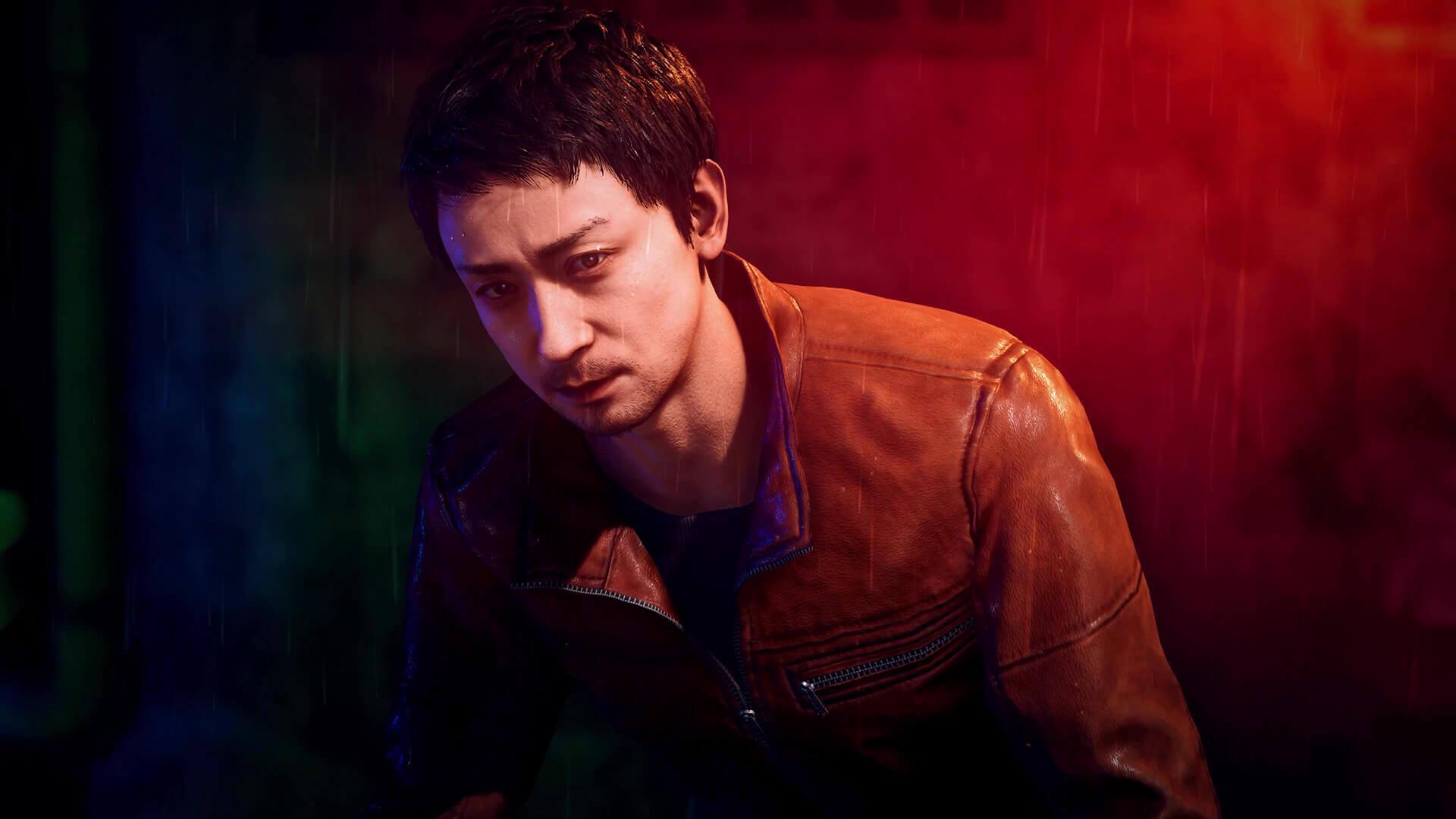 Jin Kuwana, a man with stubble in a worn brown leather jacket, leans forward under red and green light
