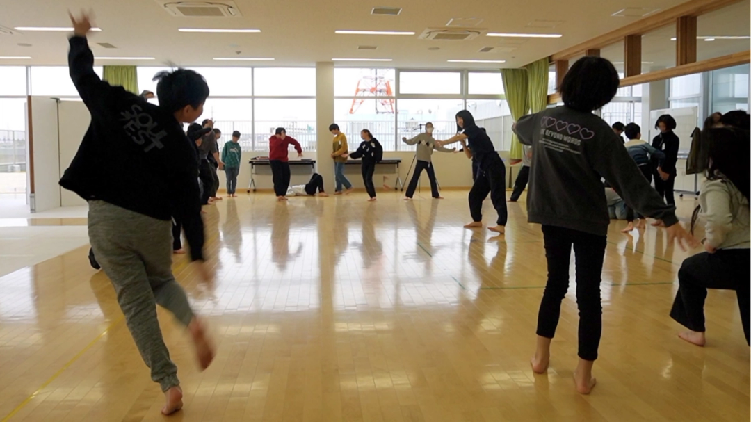 明るいスタジオで、参加者たちが身体を大きく動かしながら行うダンスワークショップの様子