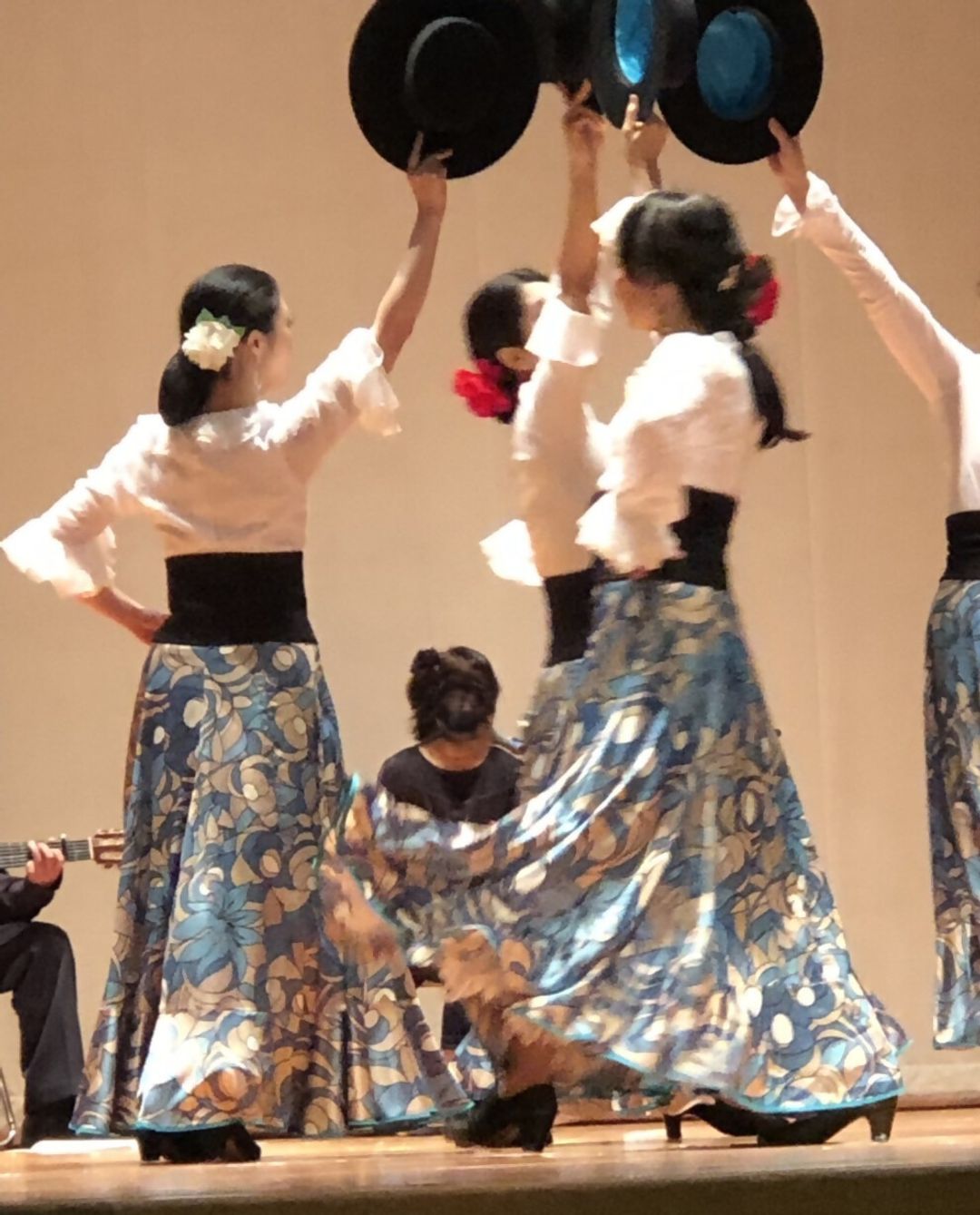青い花柄のロングスカートを身につけ、帽子を掲げながらフラメンコを踊る女性たち
