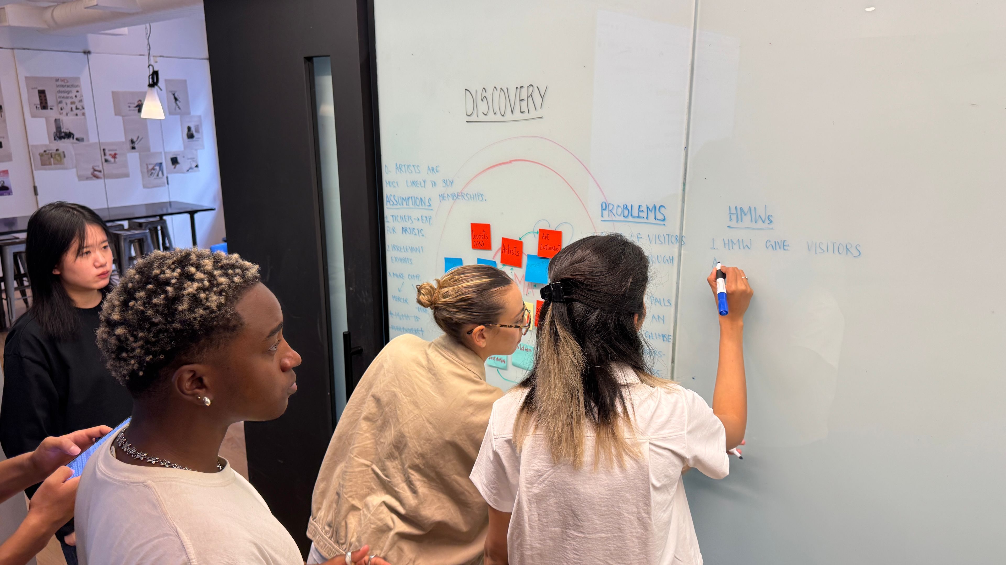 A group of students gathered in a classroom, writing on a whiteboard with marker.