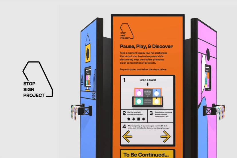 Concept rendering of the Stop Sign Project interactive exhibition. At left is the project's black outline logo on a light gray background. Centered is a tall, orange instructional panel titled “Pause, Play, & Discover,” explaining how visitors participate in four interactive challenges by grabbing a card, matching symbols, completing activities, collecting stickers, and scanning a QR code to discover their “buying language.” Flanking the center panel are blue and pink activity stations, each featuring mounted screens, graphic illustrations, and card dispensers holding colorful challenge cards. The three-panel installation is shown in perspective against a neutral gray background.