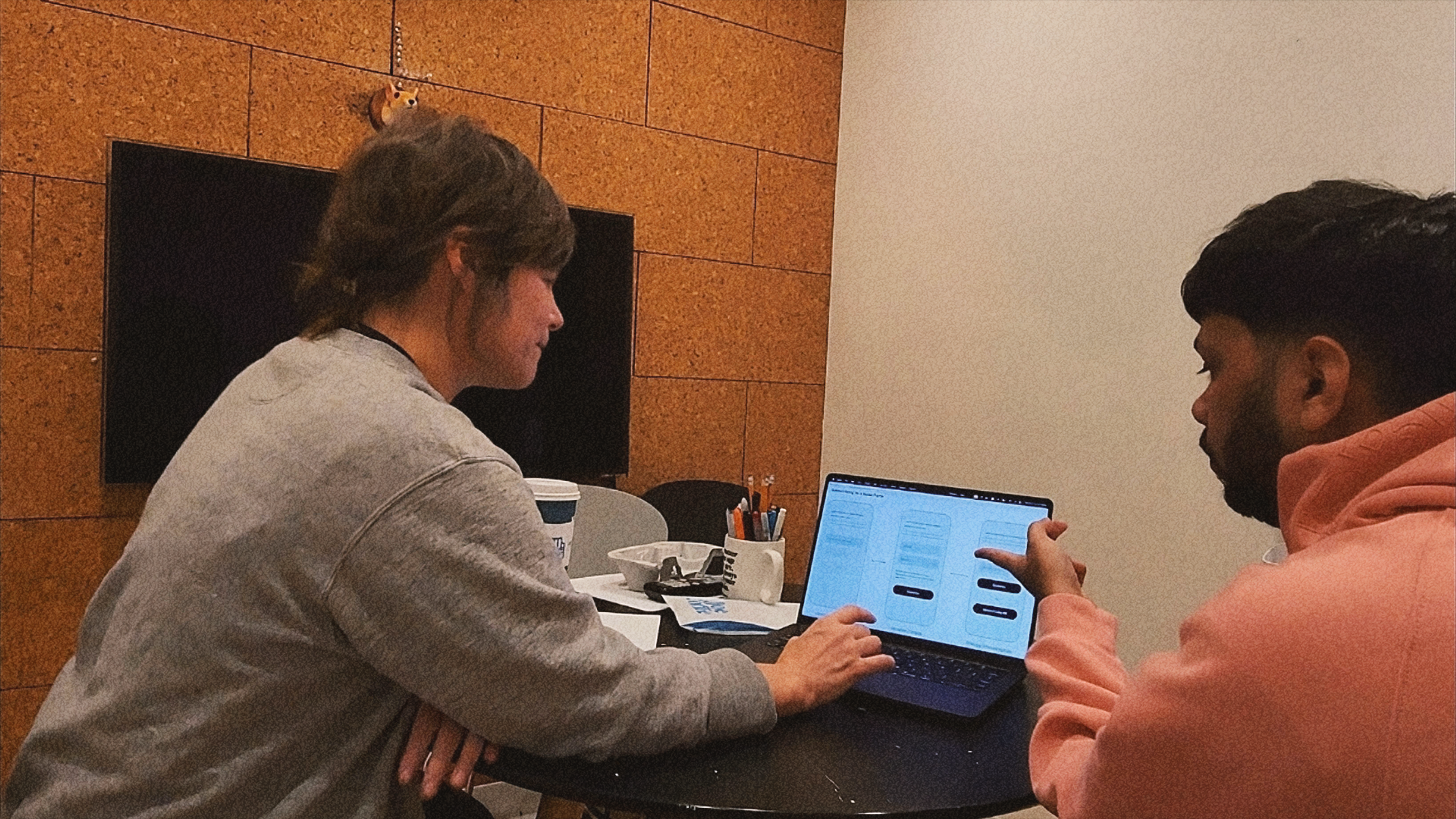 Two people collaborate at a table, reviewing wireframes and interface designs on a laptop during a design work session.