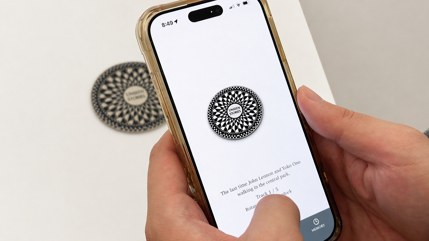 Hands holding a phone with an abstract black and white symbol containing the words 'Unseen Stories'.