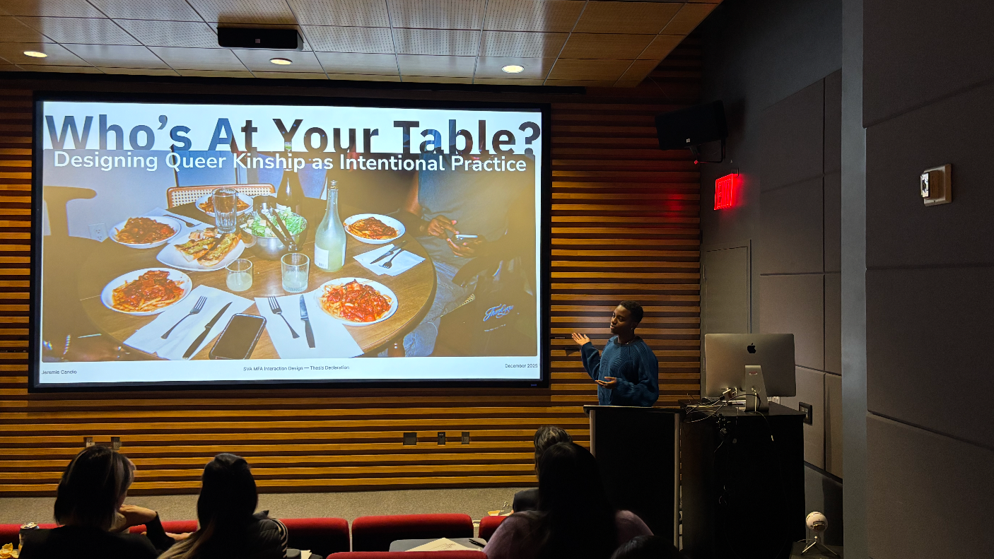 Student presenting their work in the SVA theater. The words Who's At Your Table? and a photo of a dinner table are projected on a large screen as he speaks.