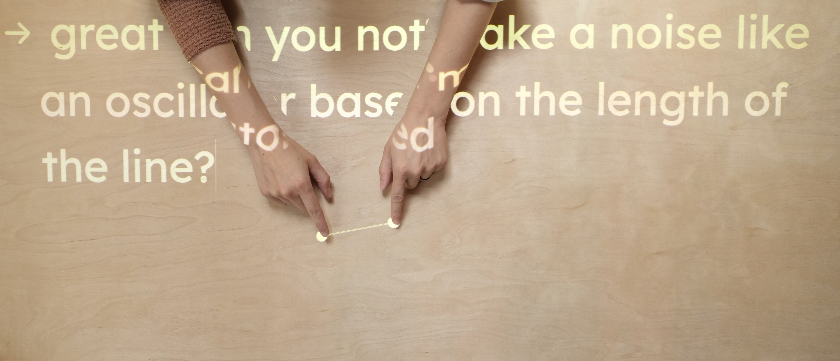 Image of hands activating a projection using Procession. Text projected over the hands reads: Can you make a noise like an oscillator based on the length of the line?
