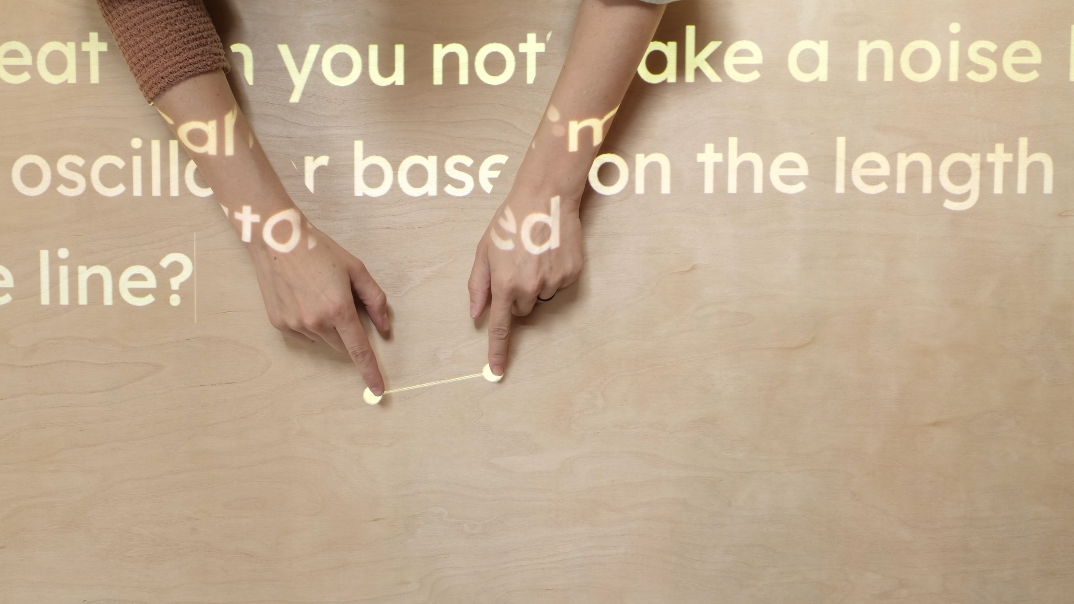 Image of hands activating a projection using Procession. Text projected over the hands reads: Can you make a noise like an oscillator based on the length of the line?