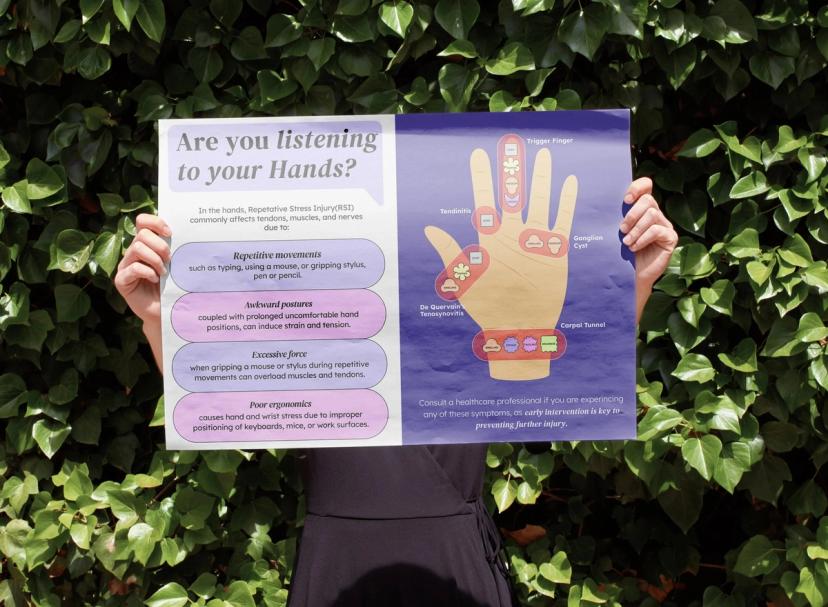 A person holds an educational poster about repetitive stress injuries (RSI) in the hands, explaining common causes, symptoms, and hand-related conditions.