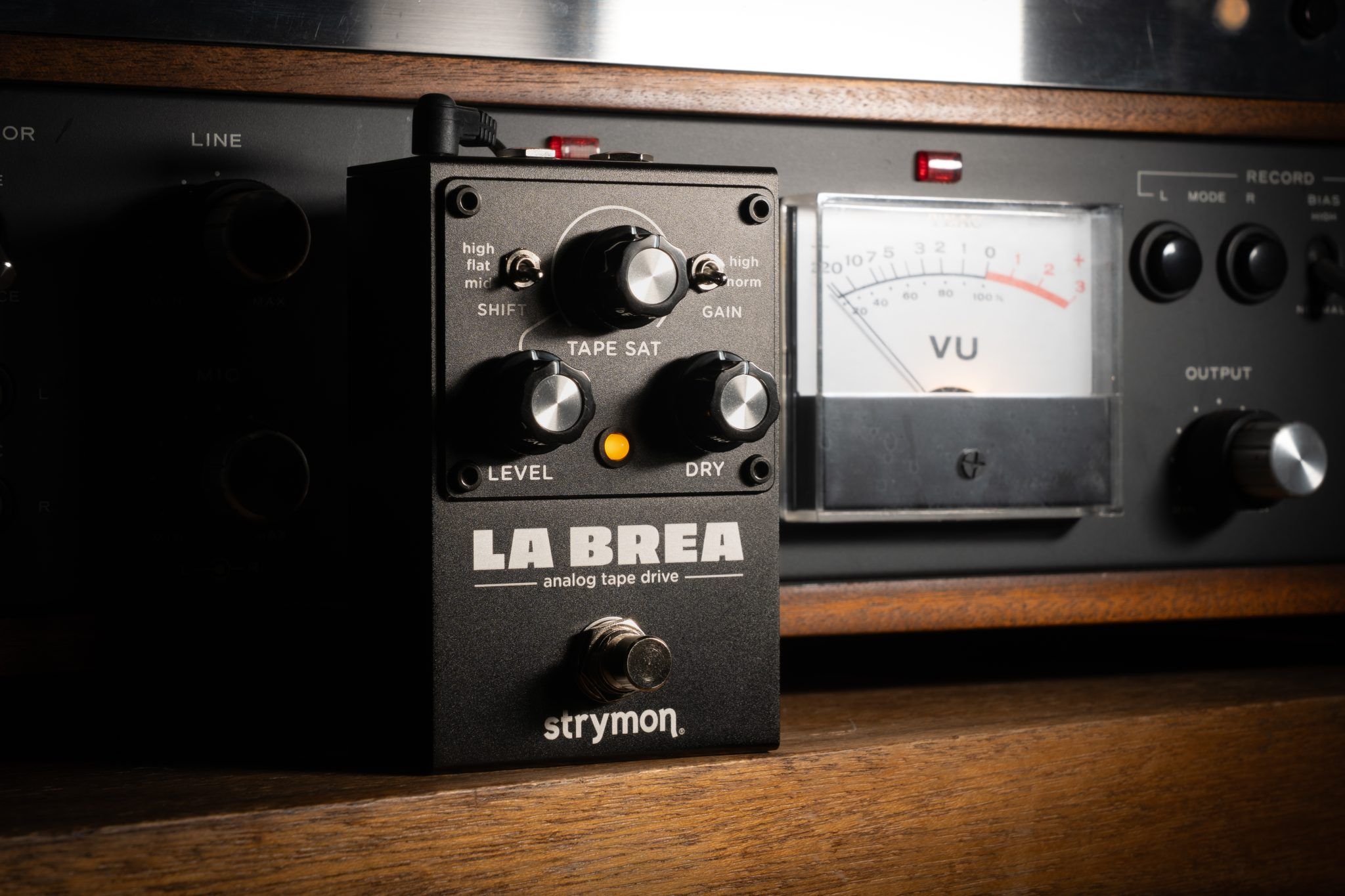 Strymon La Brea analog tape drive on a wooden shelf in front of a TEAC tape machine VU meter