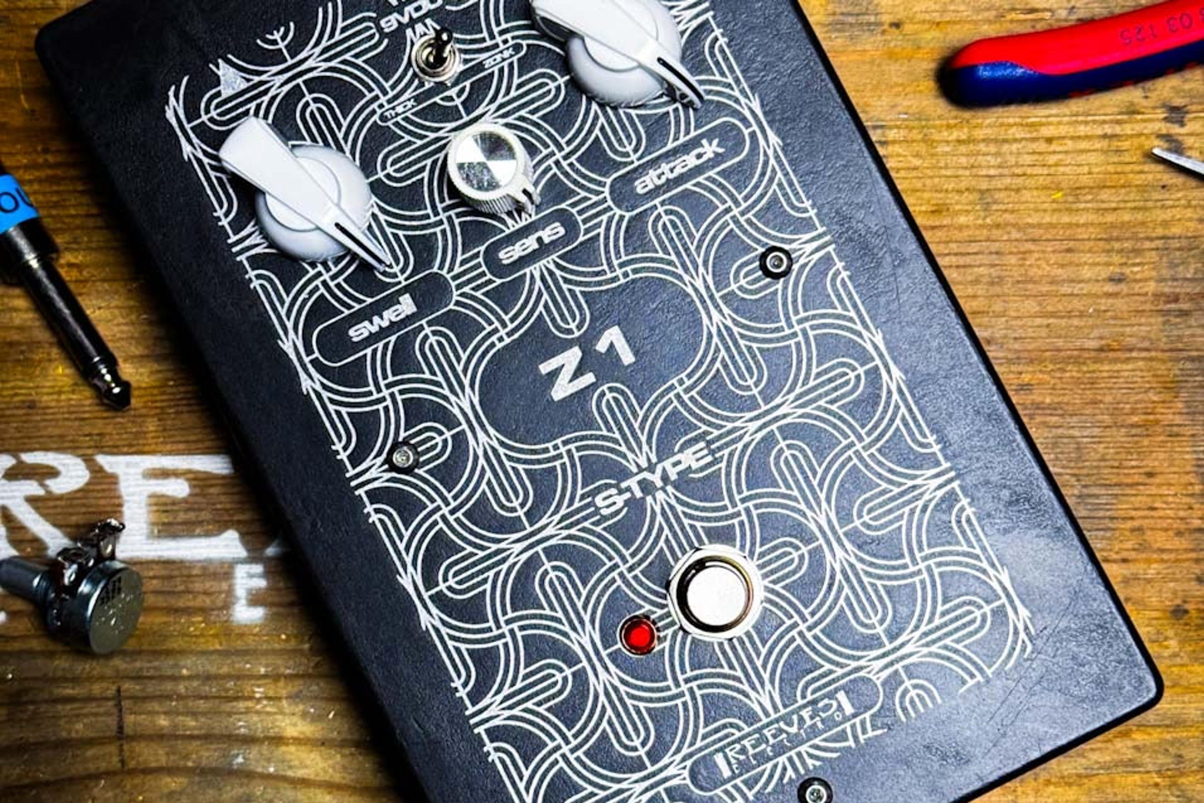 Reeves Electro Z1 fuzz on a wooden workbench among pliers and tools, black acid-etched enclosure with three white knobs and a red LED