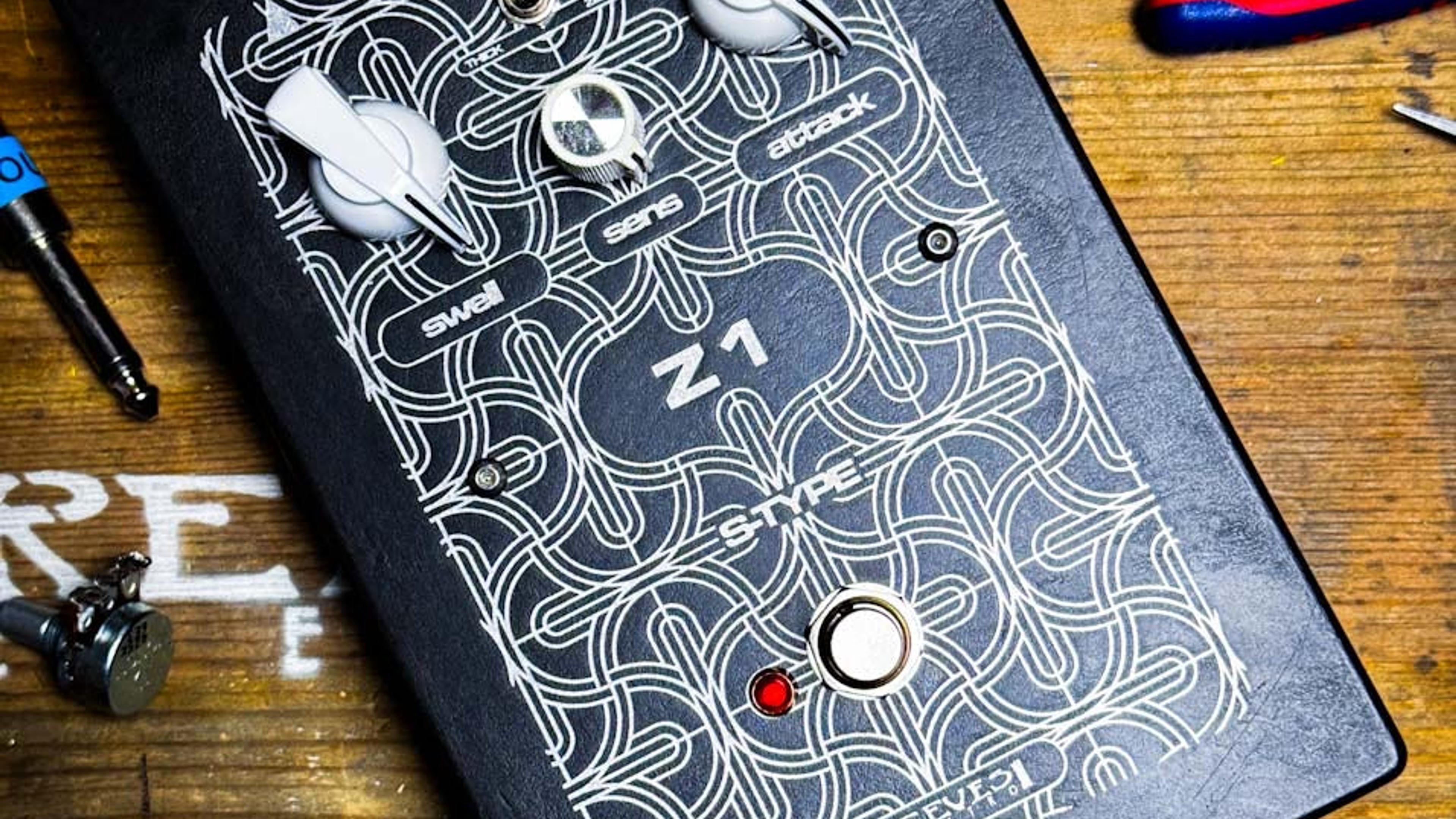 Reeves Electro Z1 fuzz on a wooden workbench among pliers and tools, black acid-etched enclosure with three white knobs and a red LED