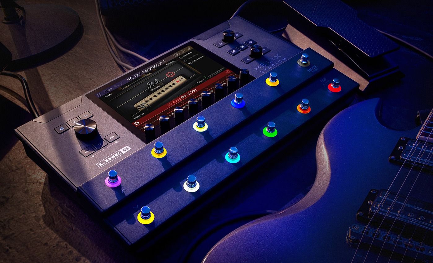 Line 6 Helix Stadium Floor on a dark stage floor beside an electric guitar, touchscreen showing the Brit SL100 amp block